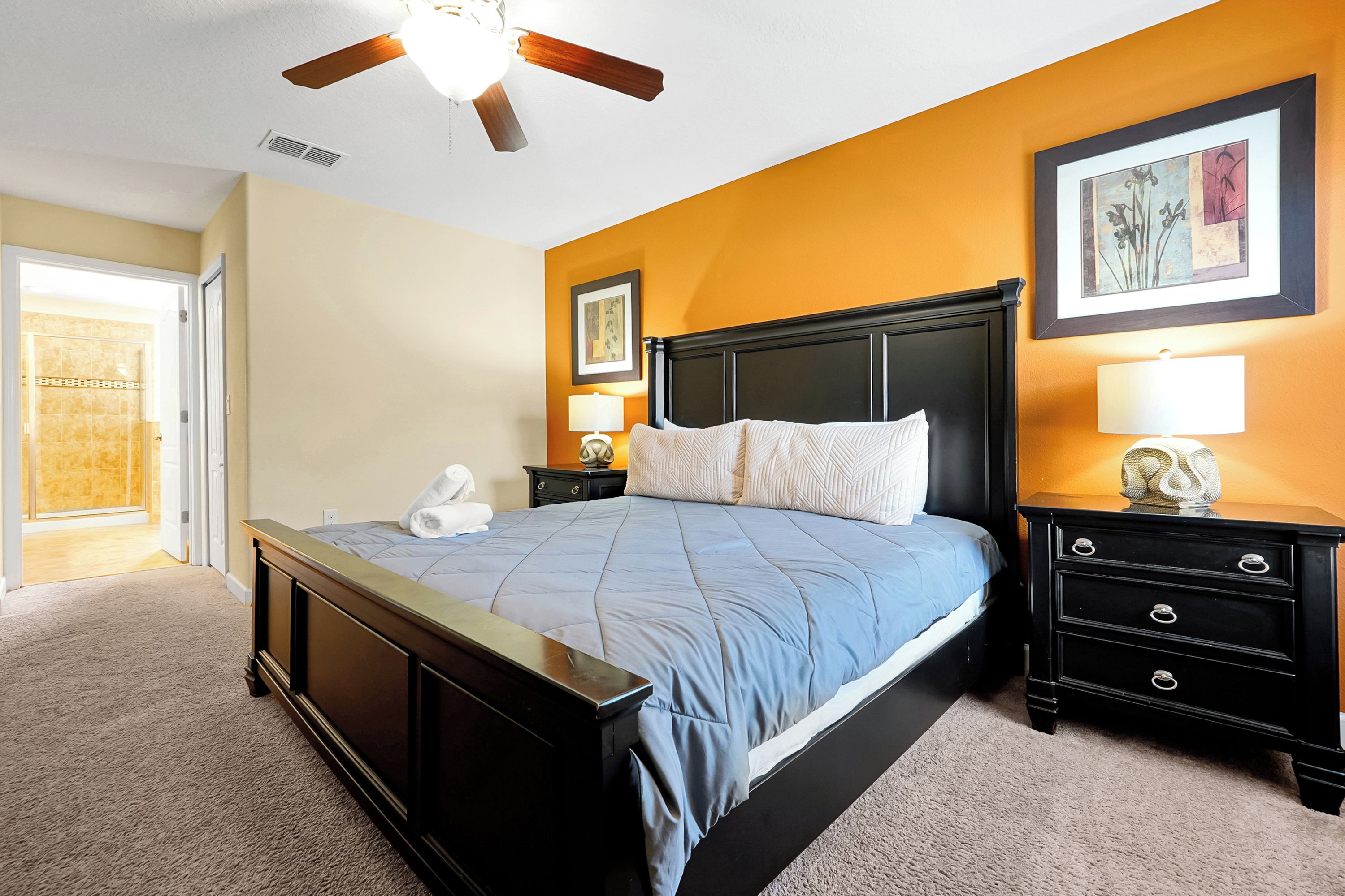 A bedroom with a bed, nightstands, a ceiling fan, and artwork on the walls.