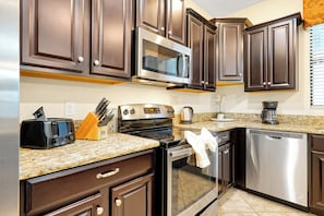 A modern kitchen with dark wood cabinets, stainless steel appliances, and granite countertops. - Champions Gate Pool Home | 3 King Suites | Game Room | Dog Friendly (Davenport)