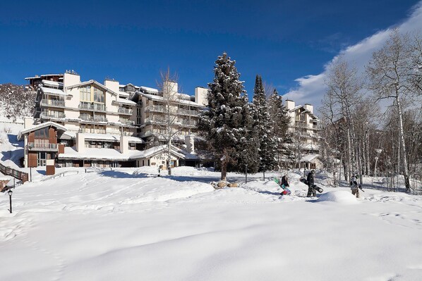 A snow-covered mountain resort with multi-story buildings, ski slopes, and snow-covered trees.