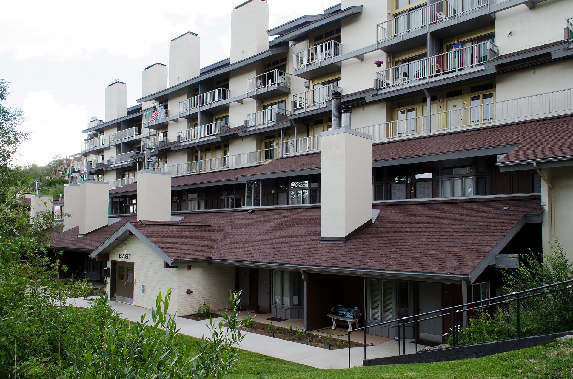 A multi-story residential building with balconies, a covered outdoor area, and a small garden.