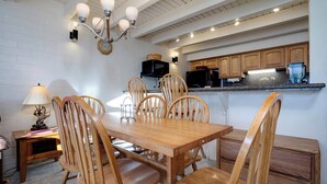 Un coin repas avec une table et des chaises en bois, un lustre et une cuisine en arrière-plan.