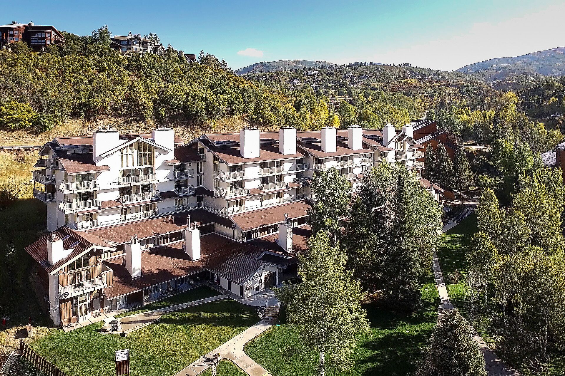 A multi-story hotel with balconies, surrounded by trees and hills.