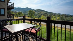 En balkon med et bord og stole, med udsigt over et bjergrigt landskab.