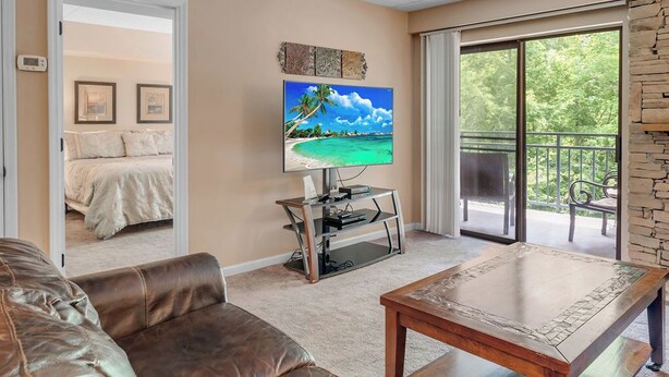 Una sala de estar con un televisor grande, un sofá de cuero, una mesa de centro de madera y un balcón con pared de piedra.