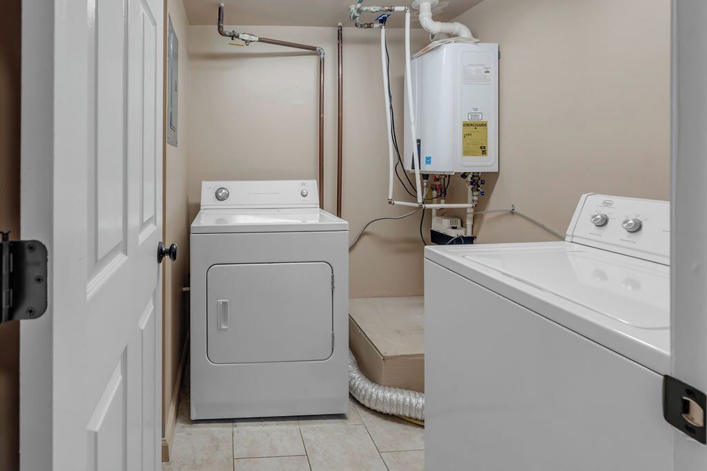A laundry room with a front-loading washer, a stacked dryer, and a water heater.