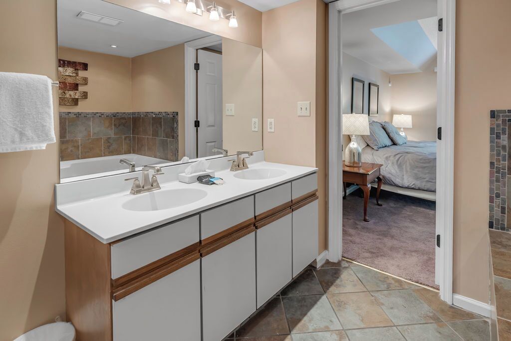 Un baño moderno con dos lavamanos, un espejo grande y vistas al dormitorio.