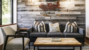 Una sala de estar con un sofá gris, almohadones a rayas, una mesa de centro de madera y una pared rústica con un cartel que dice 'Parkes Station'.