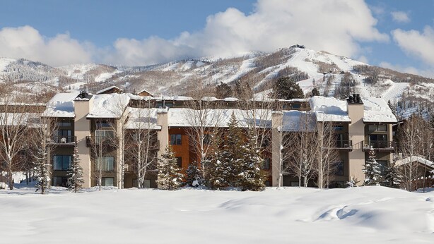 Un hotel de varios pisos con un paisaje nevado y montañas al fondo.