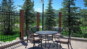 Un patio al aire libre con una mesa redonda y cuatro sillas, rodeado por una valla de metal y árboles.