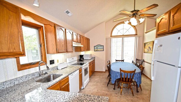 A kitchen with granite countertops, wooden cabinets, a dining table with chairs, a ceiling fan, and a refrigerator. - Fountain Road 13701-Bayside 137th St, W/D, AC (Ocean City)