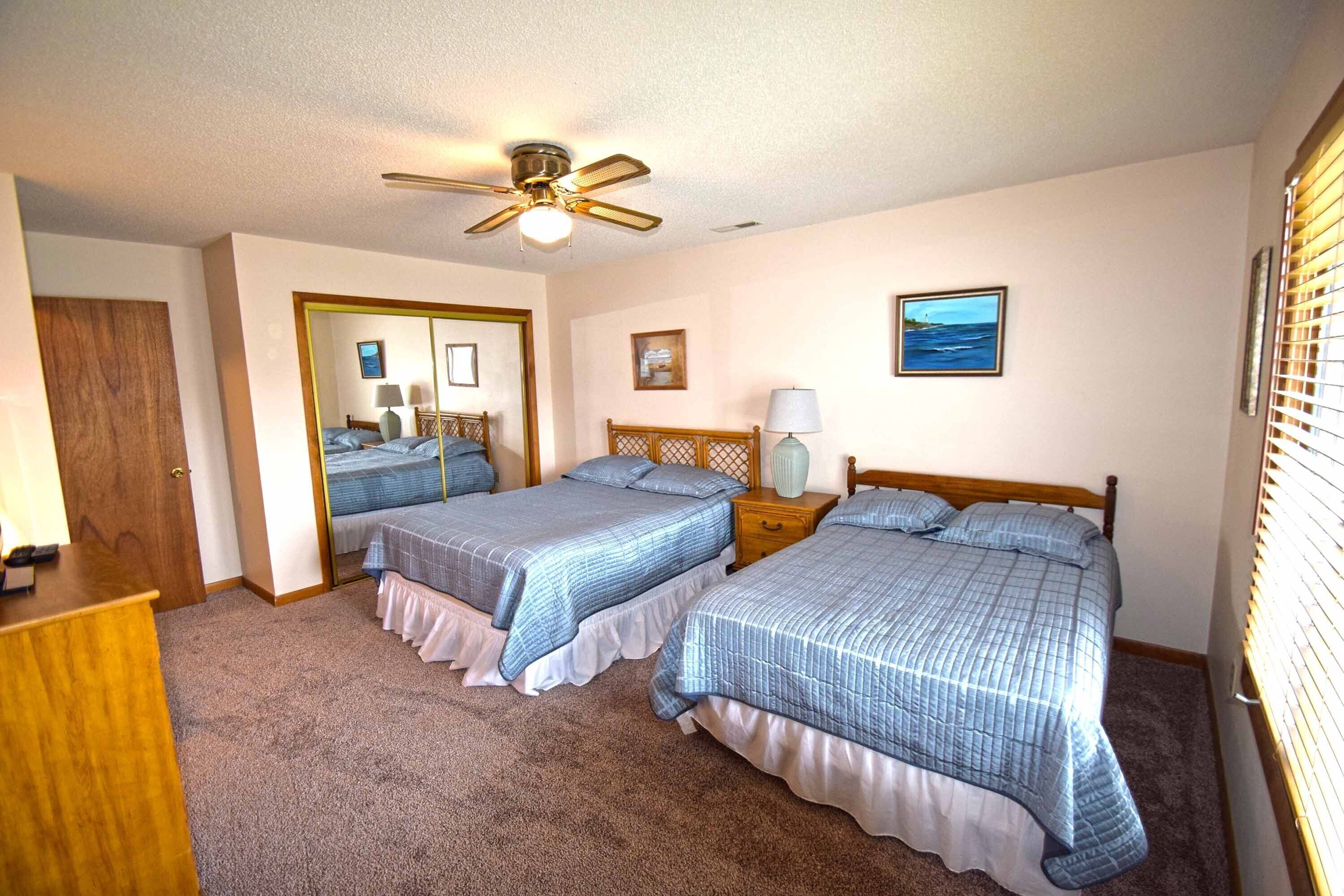 A bedroom with two beds, a ceiling fan, a mirror, and a window with blinds.