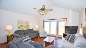 A living room with a grey sofa, a white sofa, a striped armchair, a coffee table, a TV, and a ceiling fan. - Fountain Road 13701-Bayside 137th St, W/D, AC (Ocean City)