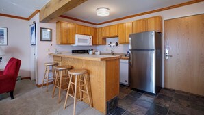 A kitchen with wooden cabinets, a stainless steel refrigerator, a microwave, and a bar stool area. - SM436 | Charming Condo | Mountain Views | Hot Tub | Ski In | Free City Bus (Steamboat Springs)