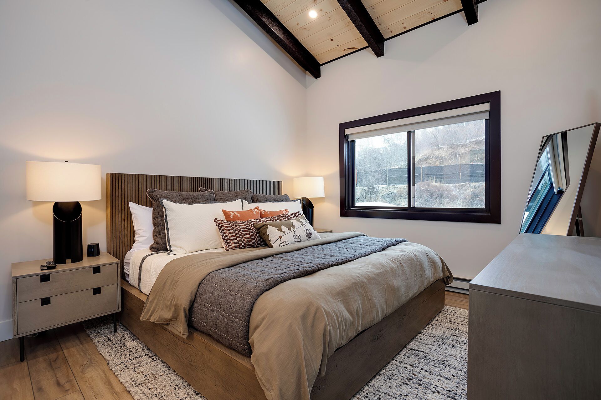 A bedroom with a bed, bedside tables, a window, and a wooden ceiling.