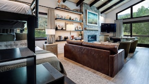 A modern living room with a stone fireplace, a television, and a large window offering a view of the outdoors.
