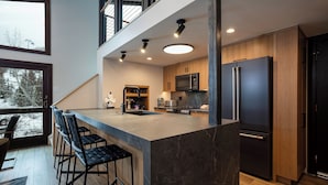 A modern kitchen with a large island, bar stools, a refrigerator, and a microwave.