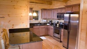 A wooden cabin kitchen with a granite countertop, stainless steel appliances, and wooden cabinets. - Sunrise Ridge - Free Train Tours + Cabin + Stunning Views/Deck + Close to (Bryson City)