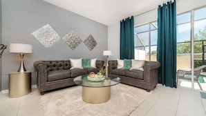 Een woonkamer met een grijze bank, twee bijzettafeltjes, een glazen salontafel en teal gordijnen.