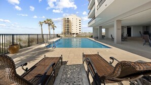 Area piscina con poltronne da relax in vimini, cielo azzurro e un edificio sullo sfondo.