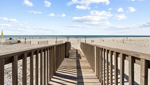 Una passerella di legno che conduce a una spiaggia sabbiosa, con cielo sereno e poche nuvole.
