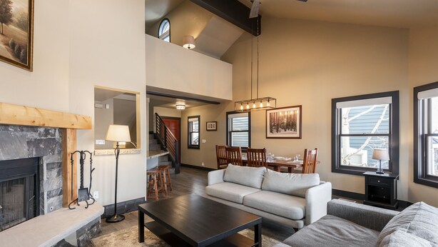 A spacious living room with a fireplace, a dining area, and a staircase leading to an upper level.