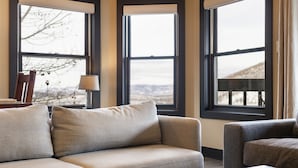A modern living room with a sofa and armchair, large windows, and a lamp.