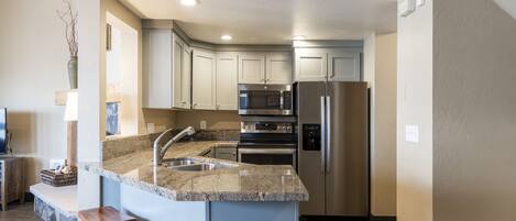 A modern kitchen with granite countertops, stainless steel appliances, and a central island with bar stools.