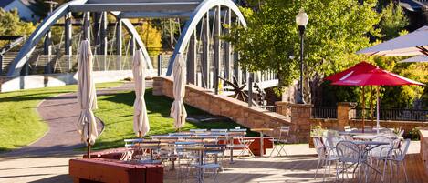 An outdoor patio area with tables and chairs, a stone pathway, and a bridge in the background.