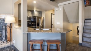 A kitchen with granite countertops, stainless steel appliances, and wooden stools.