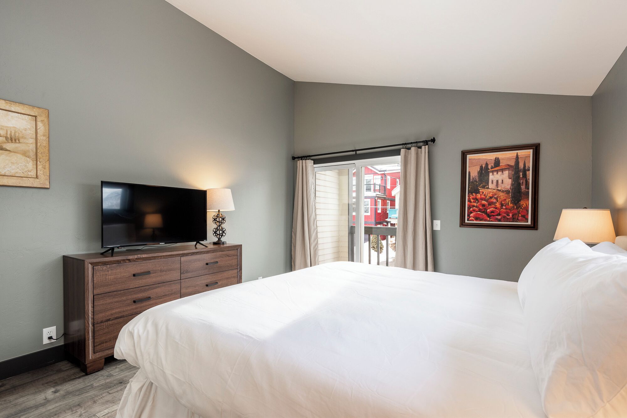 Una habitación de hotel con una cama, un televisor sobre una cómoda de madera y un cuadro en la pared.
