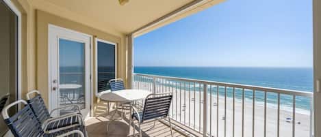 A balcony with a table and chairs, a view of the beach, and a door leading to the interior.