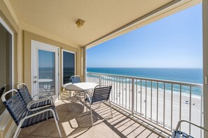 A balcony with a table and chairs, a view of the beach, and a door leading to the interior. - Beachfront Coastal Condo | Sleeps 6 | Pool | On-Site Dining (Gulf Shores)