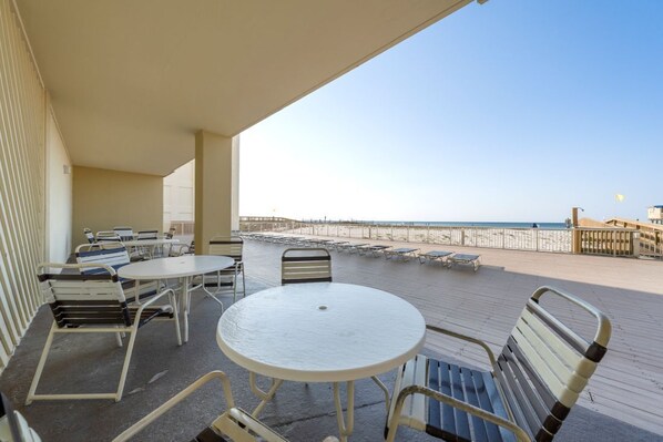 A covered outdoor area with tables and chairs, a view of the beach, and a wooden deck. - Beachfront Coastal Condo | Sleeps 6 | Pool | On-Site Dining (Gulf Shores)