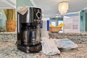 A kitchen with a coffee maker, a basket of fresh herbs, and a welcome sign.