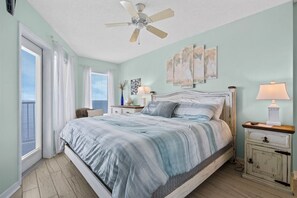 A bedroom with a bed, a ceiling fan, a nightstand with a lamp, and artwork on the wall.