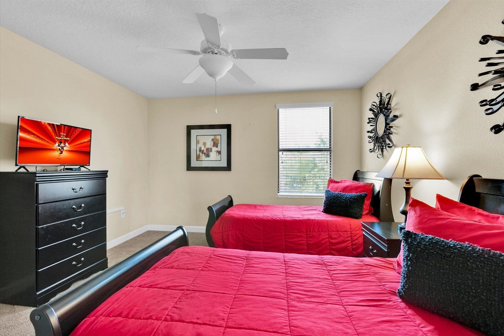 A bedroom with two beds, a ceiling fan, a dresser, a TV, and a window with blinds.
