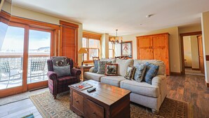 A spacious living room with a sofa, armchair, and coffee table, large windows with blinds, and a wooden cabinet. - River Run Village Walk To Gondola Pool Hot Tubs Restaurants and Shops DELUXE (Keystone)