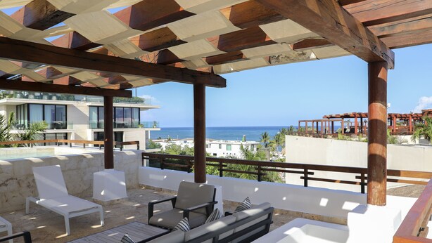 A covered outdoor seating area with lounge chairs and a sofa, overlooking a pool and ocean view. - 2 BR Ocean View PH- Jacuzzi and Private Pool steps from Mamitas Beach (Playa del Carmen)