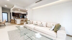 A modern living room with a sofa, glass coffee table, and a kitchen area in the background. - 2 BR Ocean View PH- Jacuzzi and Private Pool steps from Mamitas Beach (Playa del Carmen)