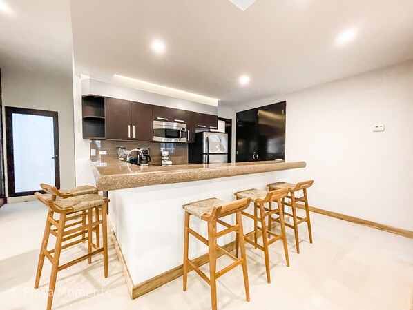 A modern kitchen with a central island and bar stools, equipped with stainless steel appliances.