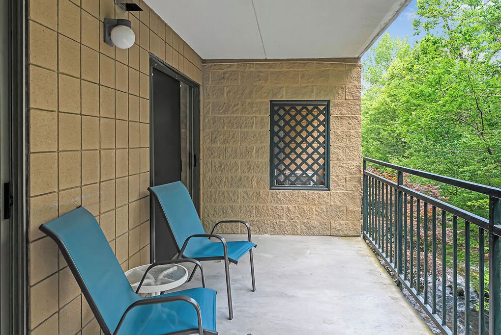A balcony with two blue chairs, a small table, and a lattice window.