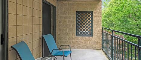 A balcony with two blue chairs, a small table, and a lattice window.