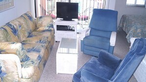 Una sala de estar con un sofá, un sillón azul, una mesa de centro y un televisor sobre un mueble.