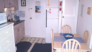 Cocina compacta con refrigerador, microondas y cafetera. Hay una mesa de comedor con sillas y un tazón azul sobre ella.