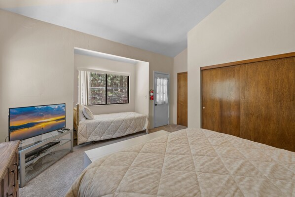 A bedroom with a TV, two beds, a window with a view, a door, and a wooden wardrobe. - Summit X-ross Roads - Walk to Snow Summit, Fireplace, Deck, Barbecue (Big Bear Lake)