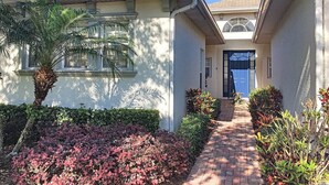 A house with a paved driveway, a blue door, and a small garden with various plants. - Rivendell: Private Pool/Spa with 24/7 Support! (Davenport)