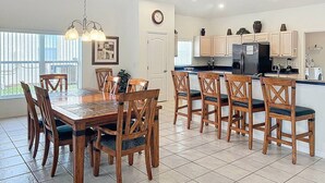 A spacious kitchen with a dining area, featuring wooden furniture, a large island, and a view of the outdoors. - Rivendell: Private Pool/Spa with 24/7 Support! (Davenport)