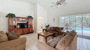 A spacious living room with a large TV, wooden entertainment unit, and a sofa set. - Rivendell: Private Pool/Spa with 24/7 Support! (Davenport)