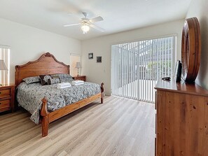 A bedroom with a wooden bed, a ceiling fan, a nightstand, a dresser, and a window with blinds.