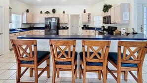 A modern kitchen with a central island, wooden chairs, and built-in appliances. - Rivendell: Private Pool/Spa with 24/7 Support! (Davenport)